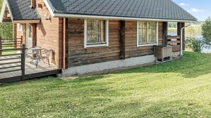 Une cabane en bois avec un toit en pente, une terrasse dotée de mobilier d’extérieur et une vue sur un lac.