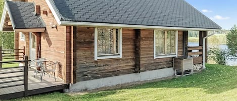 A wooden cabin with a sloped roof, a deck with outdoor furniture, and a view of a lake.