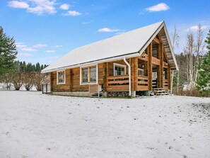 Une cabane en bois avec un toit enneigé, un porche à l’avant et un ciel dégagé.