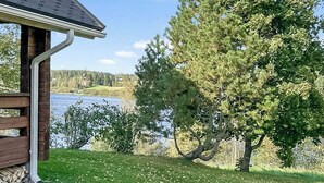 Une cabane en bois avec un toit en pente, une vue sur un lac et un grand arbre à feuilles persistantes au premier plan.