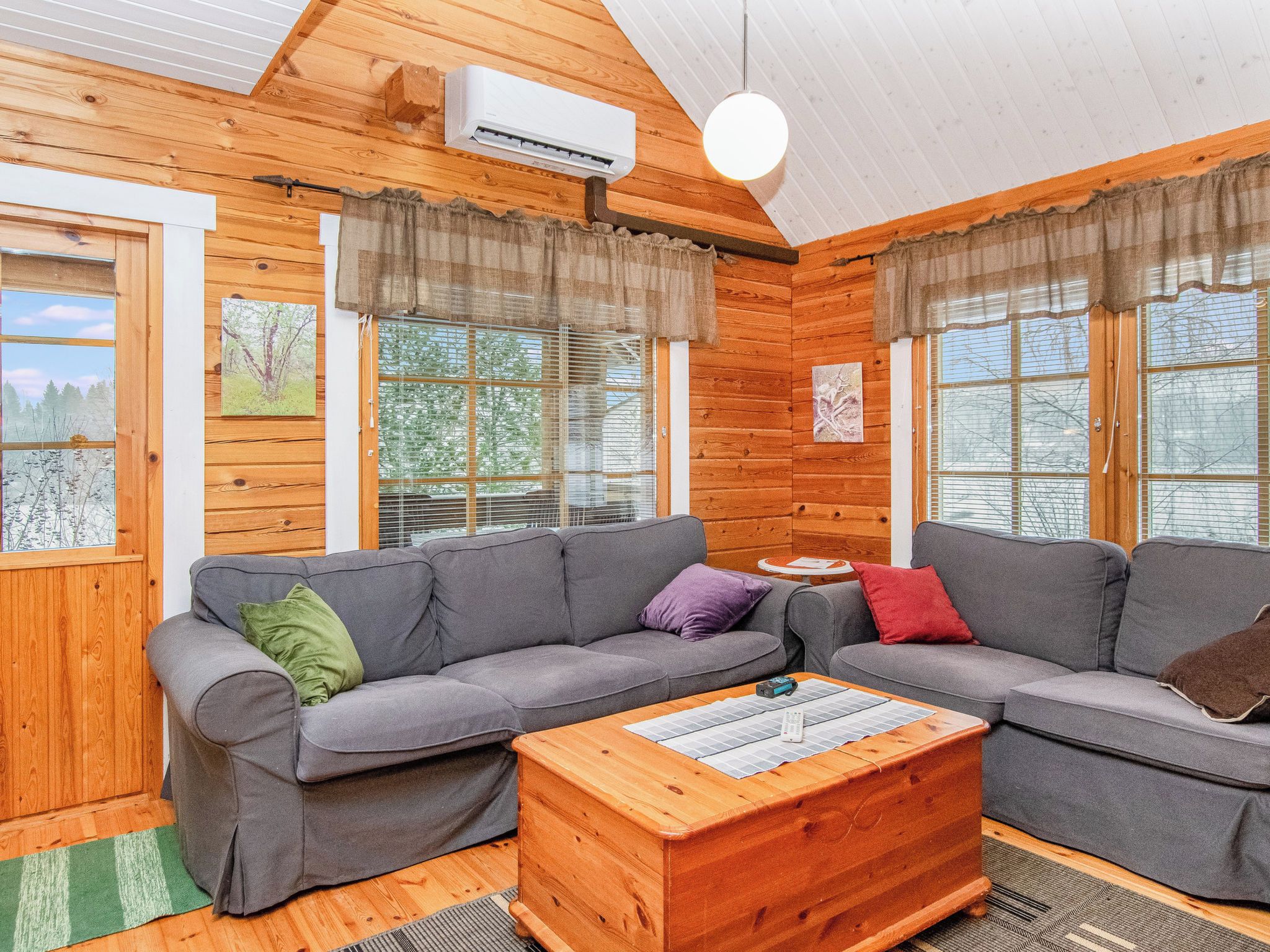 A cozy cabin interior with a grey sofa set, a wooden coffee table, and a ceiling fan.