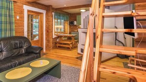 Een gezellig chaletinterieur met een houten trap, een leren bank, een eettafel en een keukenhoek.