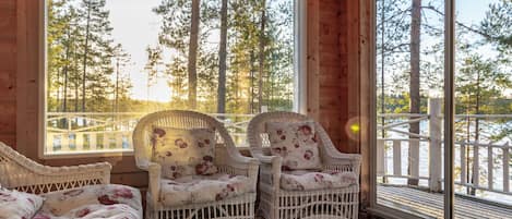 Una cabaña de madera con muebles de mimbre y grandes ventanales con vistas a un bosque.