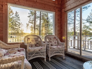 Una cabaña de madera con muebles de mimbre y grandes ventanales con vistas a un bosque.