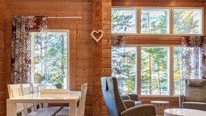 A cozy cabin interior with a dining area, two armchairs, a small table, and large windows offering a view of the forest. - Näsinjoutsen by Interhome (Ruovesi)