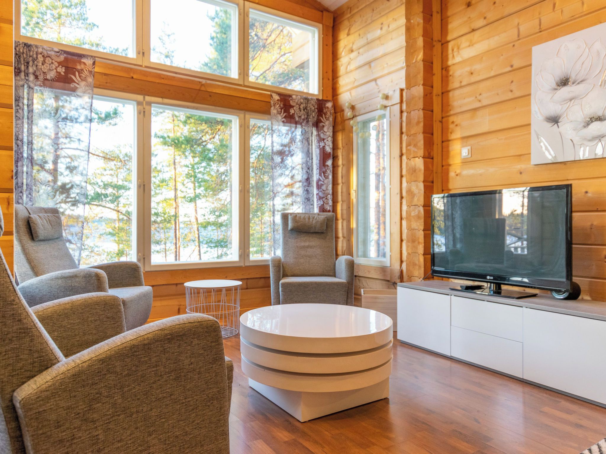 L’intérieur d’une cabane en rondins, avec un téléviseur, un coin salon et de grandes fenêtres.