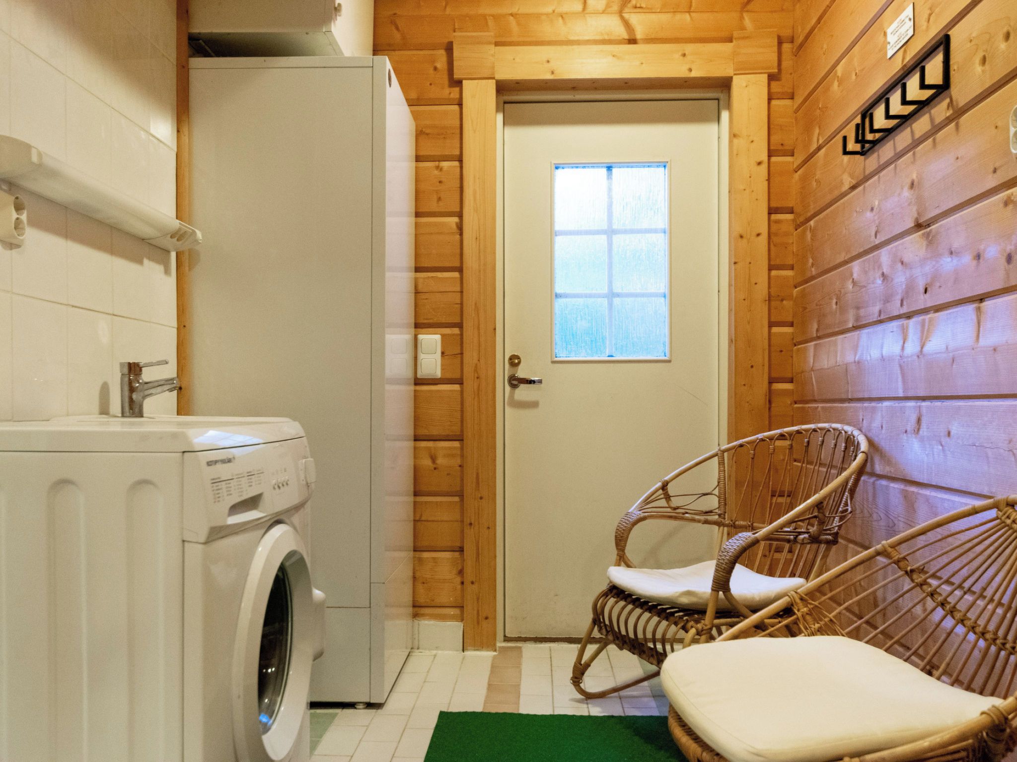 A compact room with a washing machine, a wicker chair, and a door with a window.