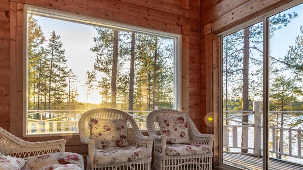 A cozy wooden cabin with wicker furniture and large windows offering a view of a forest. - Näsinjoutsen by Interhome (Ruovesi)