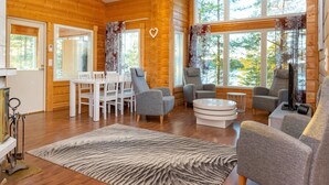 A cozy log cabin interior with a dining area, seating, and large windows offering a view of the outdoors. - Näsinjoutsen by Interhome (Ruovesi)