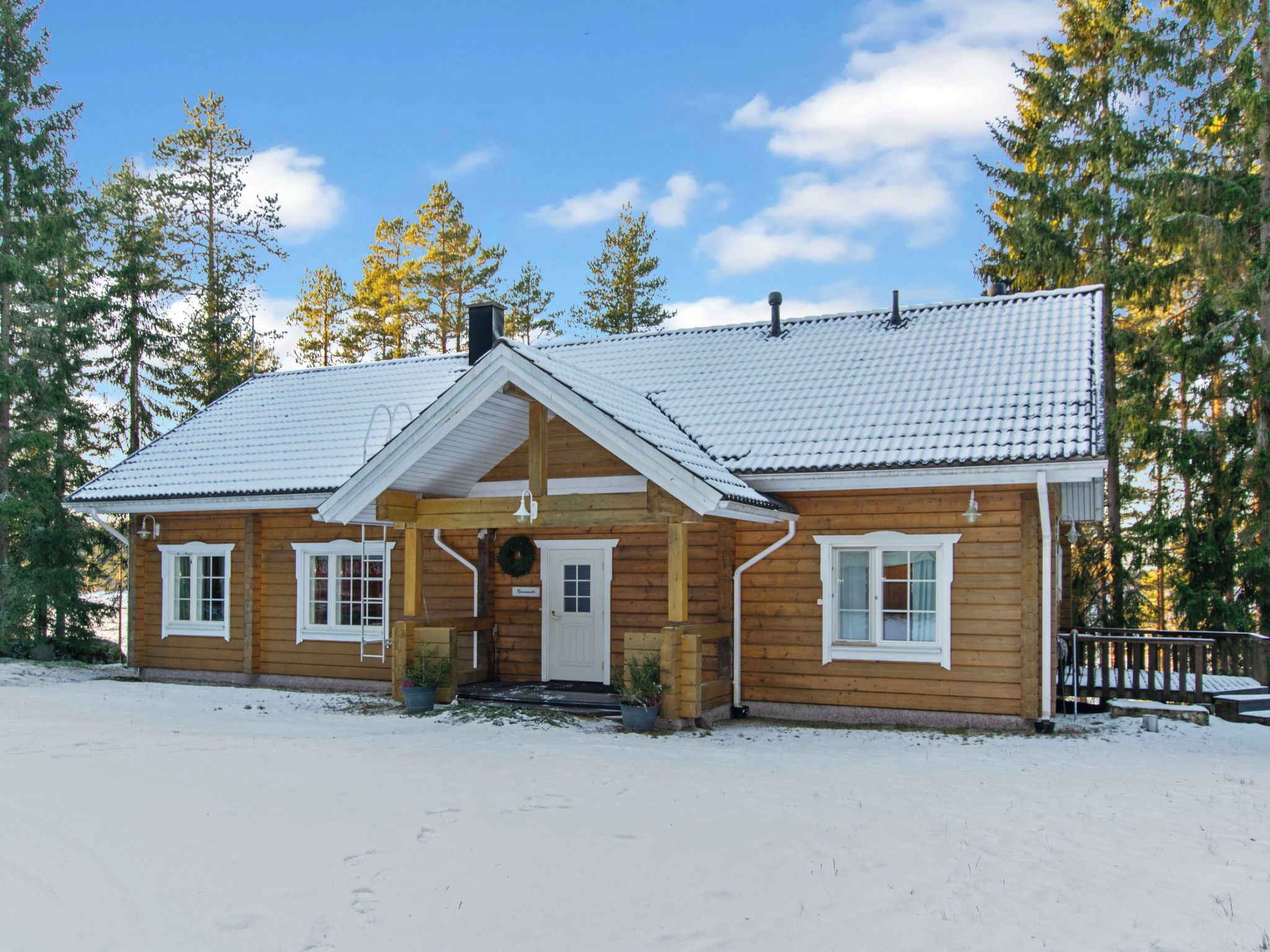 A wooden cabin with a gabled roof, a front porch, and a snow-covered ground.