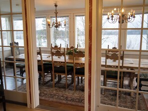 A dining area with a wooden table and chairs, a chandelier, and a view through a window with a decorative frame. - Villa rauhala by Interhome (Sastamala)