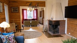 A cozy living room with a fireplace, a television mounted on the wall, and a dining area with two chairs and a table.