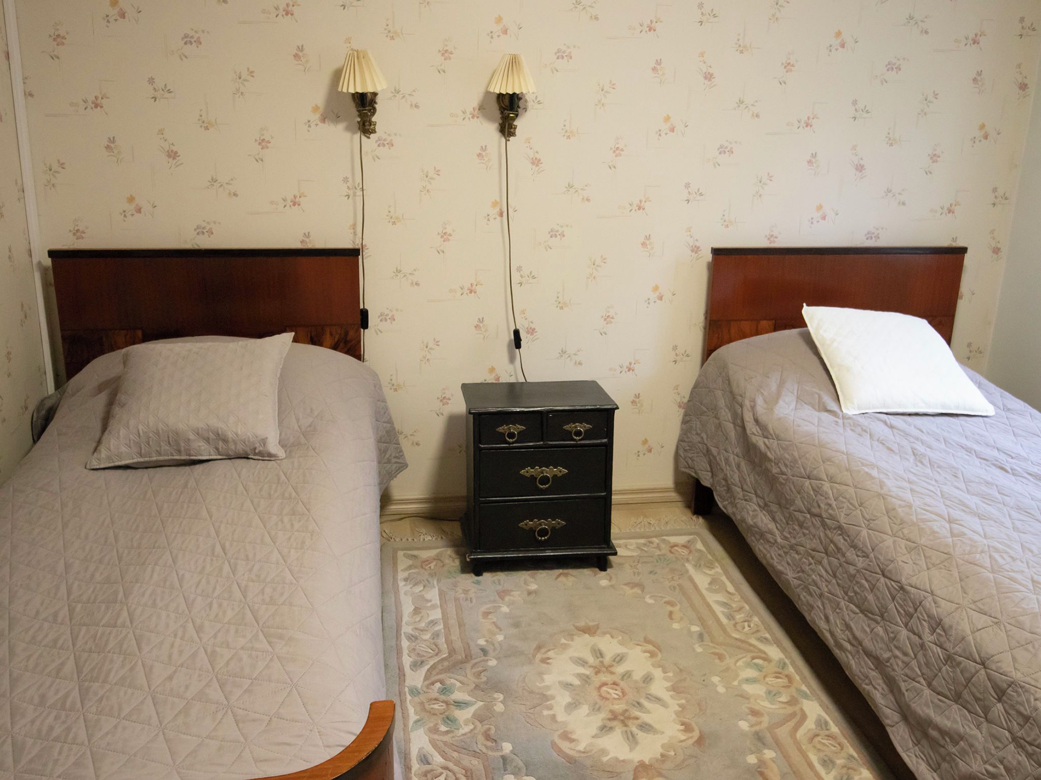 A room with two beds, a nightstand, and a wall-mounted lamp between them.