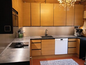 A modern kitchen with wooden cabinets, a stainless steel sink, a dishwasher, and a built-in stove. - Villa rauhala by Interhome (Sastamala)