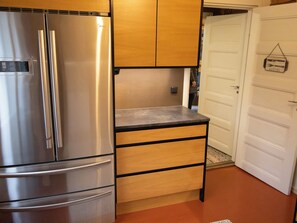 A compact kitchen with a stainless steel refrigerator, wooden cabinets, and a white door. - Villa rauhala by Interhome (Sastamala)