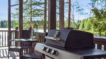 A barbecue grill on an outdoor deck with a view of a lake and trees.