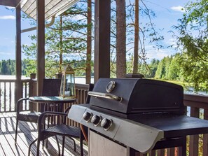 A barbecue grill on an outdoor deck with a view of a lake and trees.