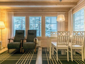 Une pièce chaleureuse avec un plafond en bois, une table à manger avec des chaises, un canapé et une fenêtre avec des stores.