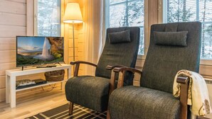 Una habitación acogedora con dos sillones tapizados, un televisor sobre un mueble blanco, una lámpara y una ventana con vistas a árboles.