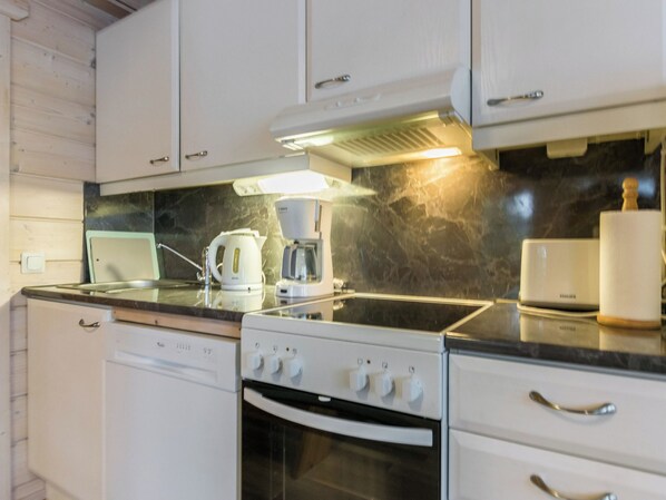 A kitchen with white cabinets, a stove, a coffee maker, and a marble backsplash.