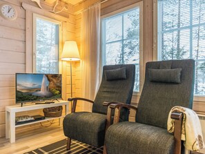 A cozy room with a television displaying a scenic waterfall, two upholstered chairs, a floor lamp, and a small white table with a basket.