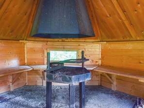 Un intérieur en bois avec un espace de cuisson central, des bancs et une fenêtre.