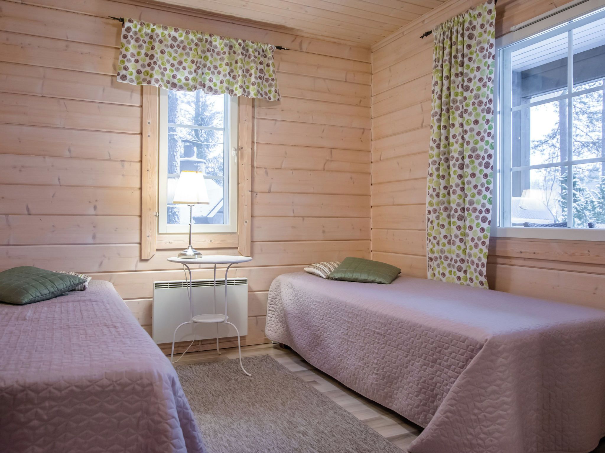 Ein gemütliches Zimmer mit zwei Betten, einem kleinen Tisch und einem Fenster mit Vorhängen.
