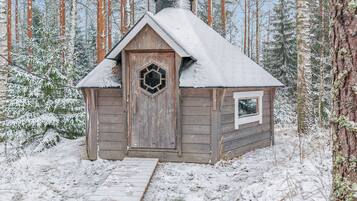 Eine kleine Holzhütte mit verschneitem Dach, einem sechseckigen Fenster und einem Schornstein.