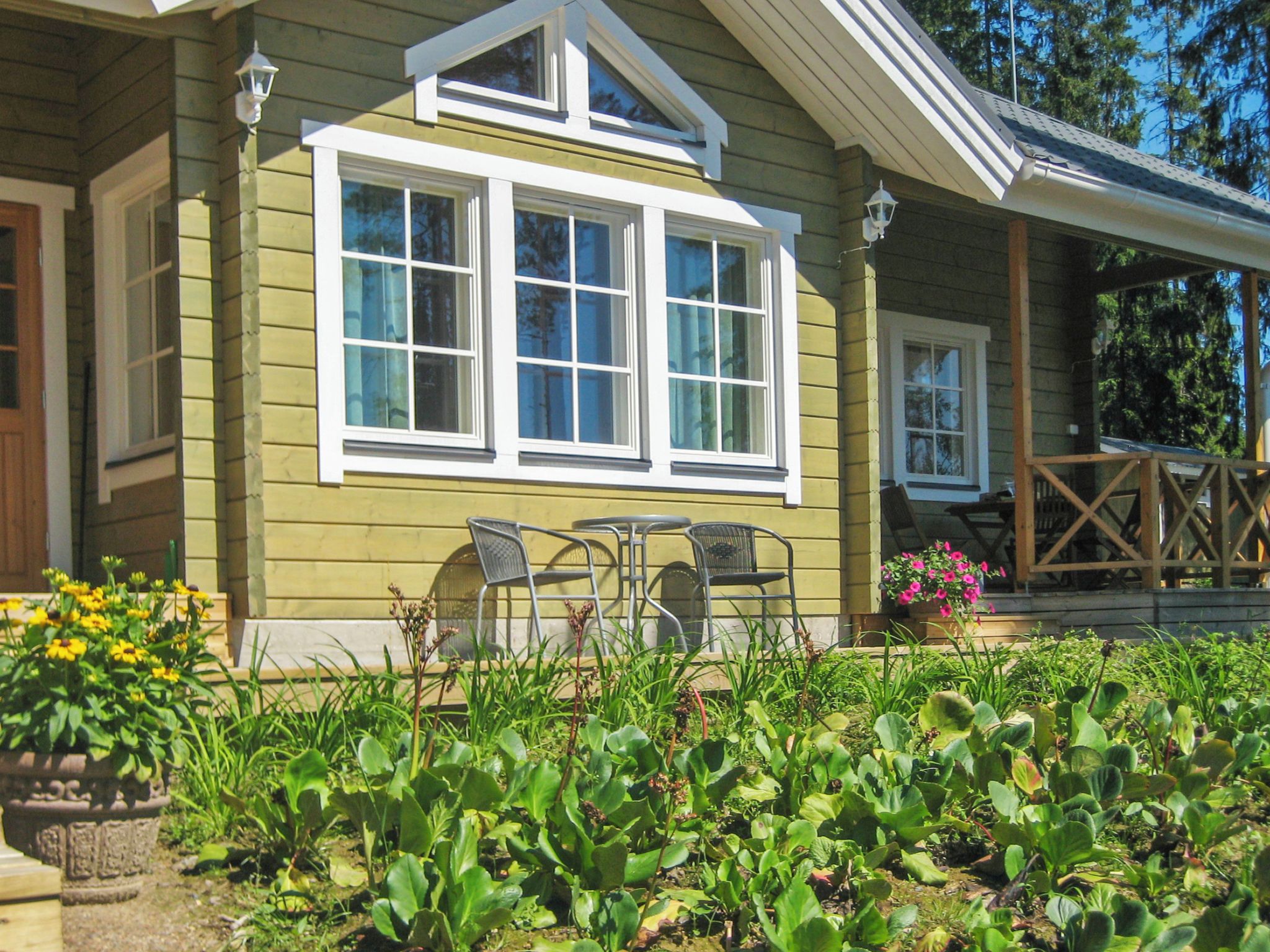 Ein Haus mit einer Veranda, einem Essbereich mit Stühlen und einem Garten mit verschiedenen Pflanzen.