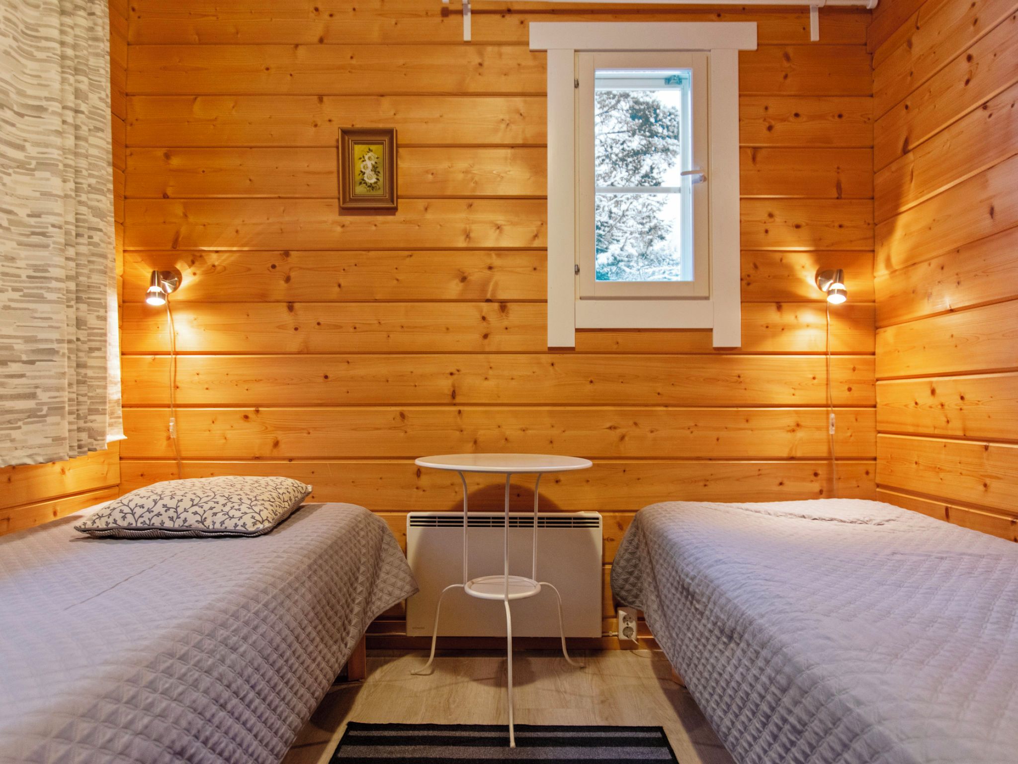 Ein gemütliches Cabin-Zimmer mit zwei Betten, einem kleinen Tisch und einem Fenster mit Blick auf Bäume.