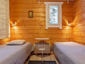 A cozy cabin room with two beds, a small table, and a window with a view of trees.