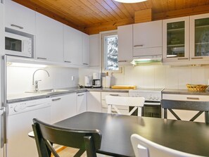 A modern kitchen with white cabinets, a stainless steel sink, a built-in oven, and a dining area with a table and chairs.