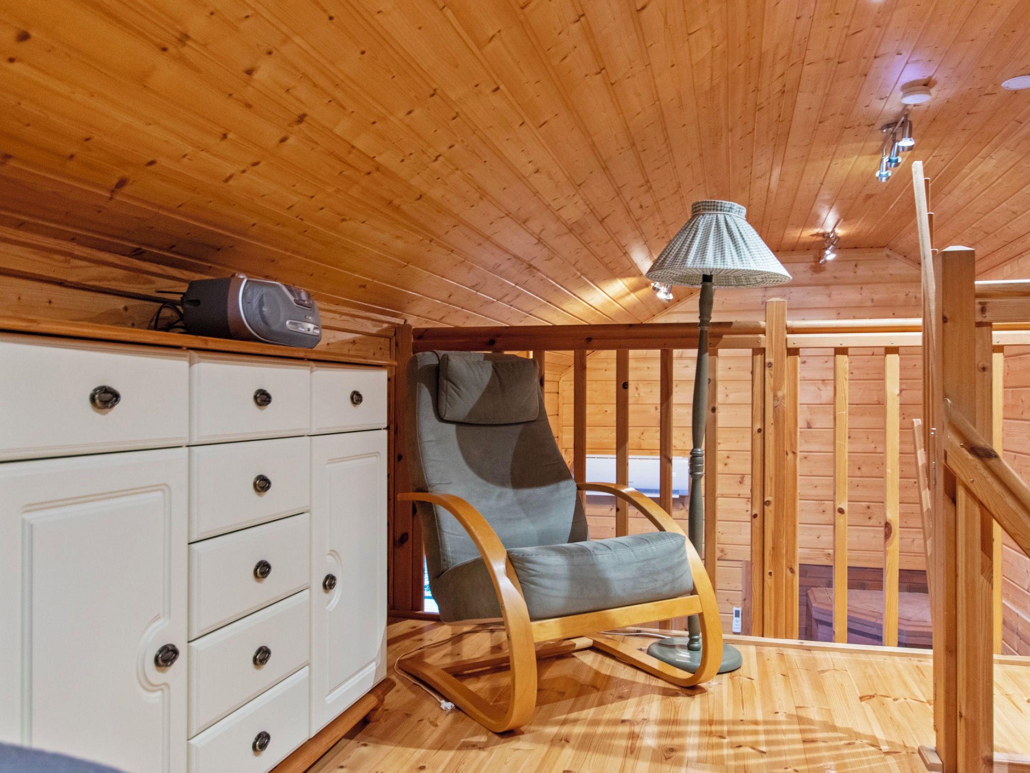 L’intérieur d’un chalet en bois, avec un fauteuil à bascule, une commode blanche à tiroirs et une lampe.