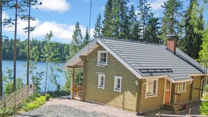 Una pequeña cabaña de madera con techo inclinado, un porche y vistas a un lago.