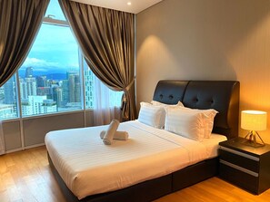 A hotel room with a large bed, a city view, and a nightstand with a lamp.