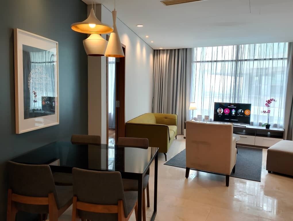 A modern hotel room with a dining area, a sofa, a TV, and a large window.