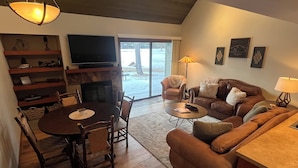 A cozy living room with a fireplace, a dining table, and a sofa. - Recently Remodeled Golf Course Condo w/ A/C, SHARC Passes, Bikes & Pet Friendly (Sunriver)