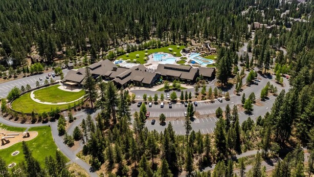 An aerial view of a resort with multiple buildings, a swimming pool, and a parking area surrounded by dense forest. - Recently Remodeled Golf Course Condo w/ A/C, SHARC Passes, Bikes & Pet Friendly (Sunriver)