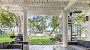 Eine überdachte Terrasse mit Korbmöbeln, einem Grill und Blick auf den Garten.