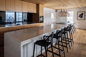 A modern kitchen with wooden cabinets, a large island with bar stools, and a dining area with a table and chairs. - Silver Dream by H2 Life (Kutchan)