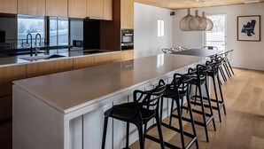 A modern kitchen with a long island, bar stools, wooden cabinets, and a hanging light fixture.