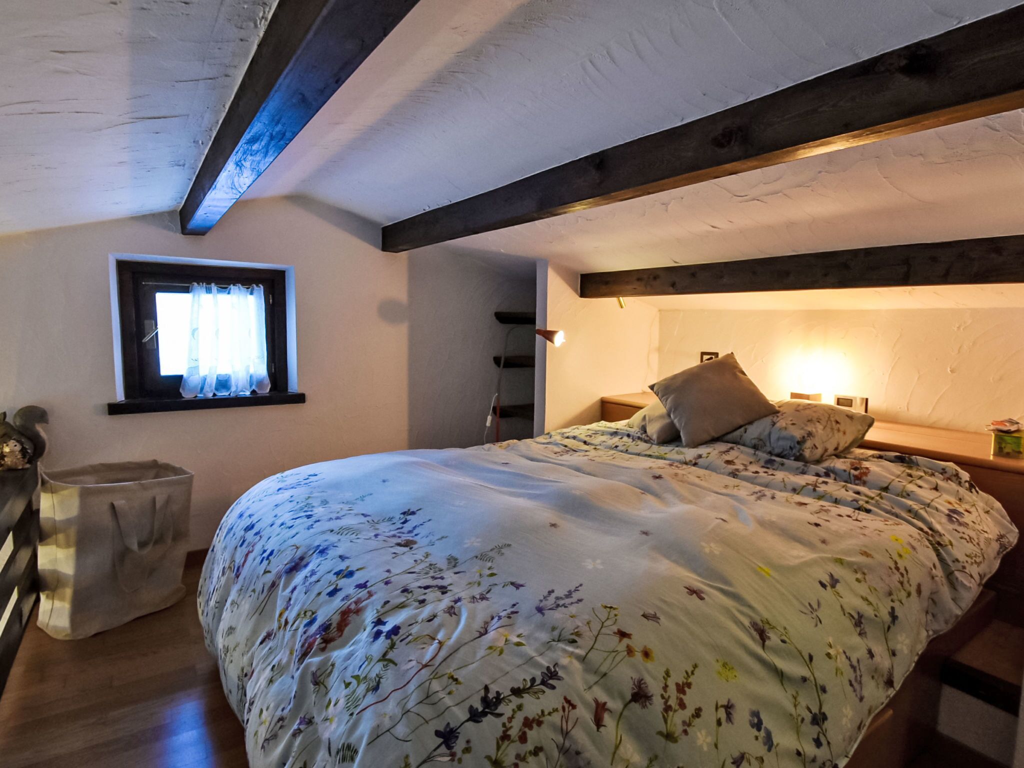 Quarto com cama, janela, mesa de cabeceira e teto de madeira.