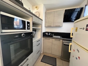 Een kleine keuken met een inbouwmagnetron, oven en koelkast, plus een klein aanrecht en kastjes.