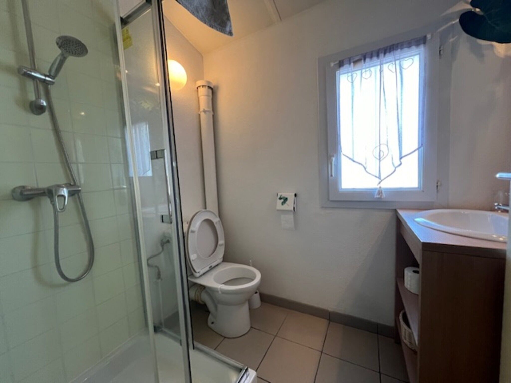 A bathroom with a glass shower enclosure, a toilet, a window with bars, and a sink.