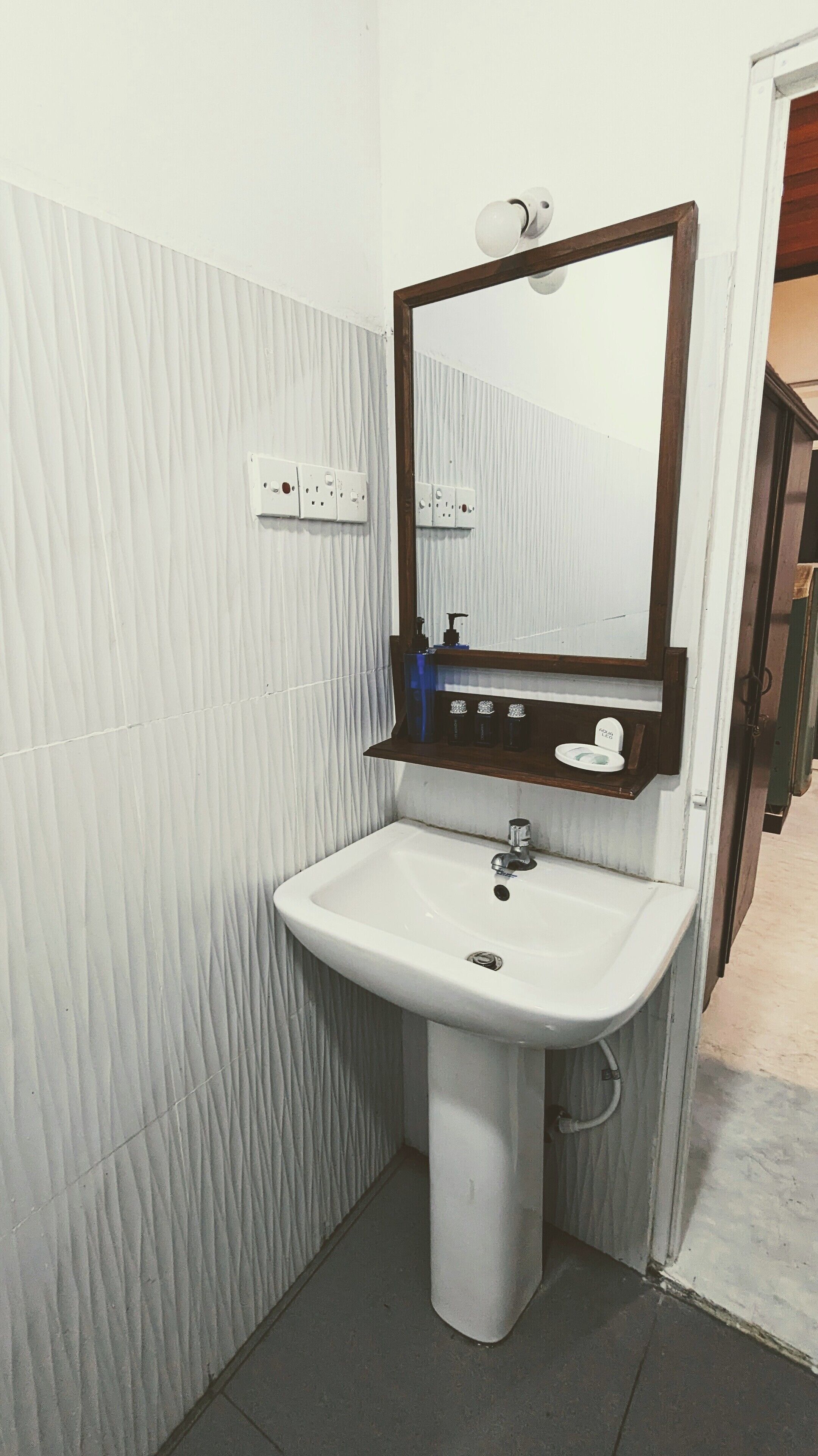 Une salle de bain avec un lavabo sur colonne, un miroir et une étagère contenant des articles de toilette.