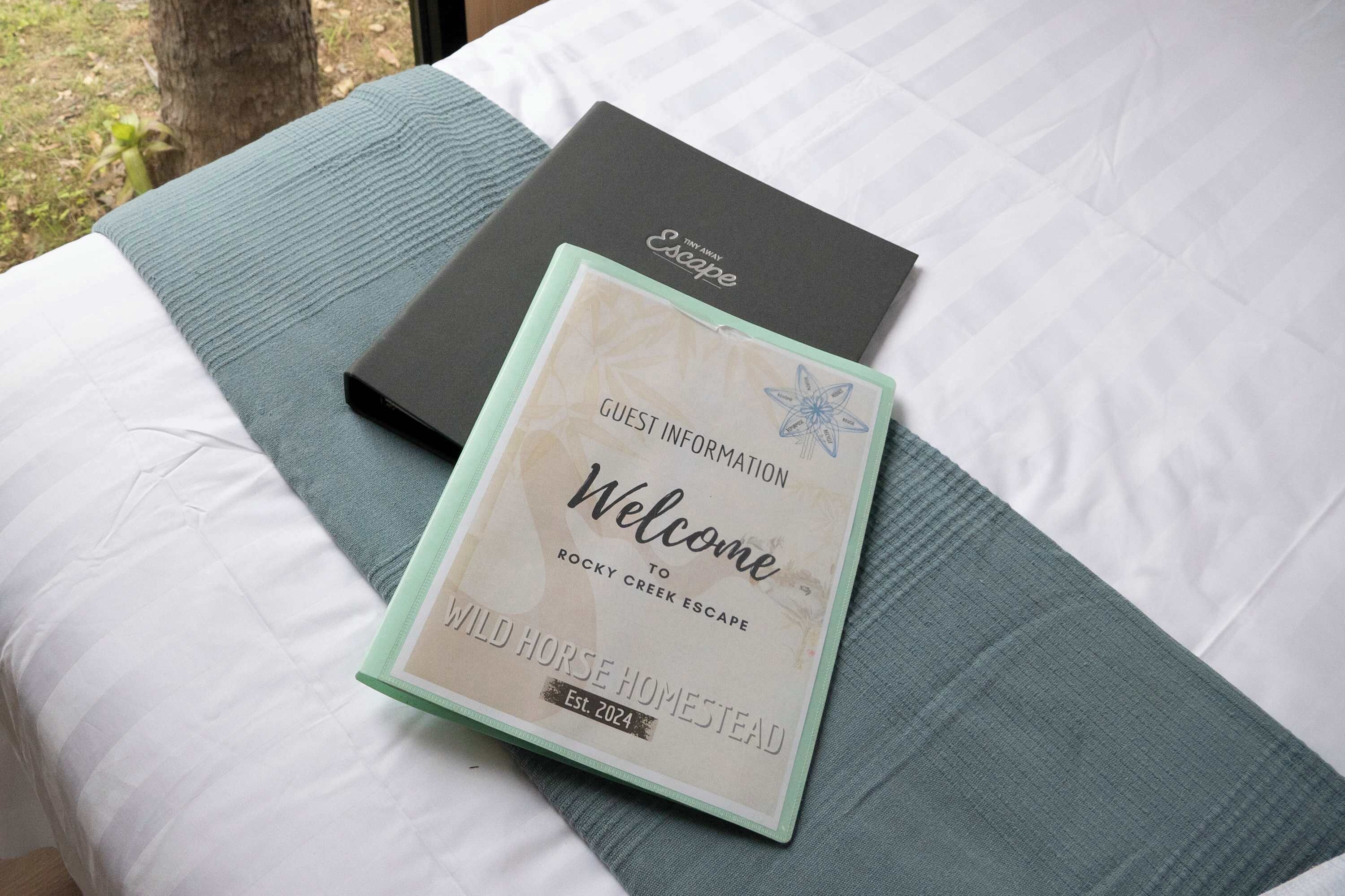 A bed with a white sheet and a green pillow, a black box labeled "Escape," and a welcome card for Wild Horse Homestead.
