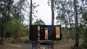 Une cabane moderne et compacte, dotée d’un foyer et de deux fauteuils, située dans une zone boisée.