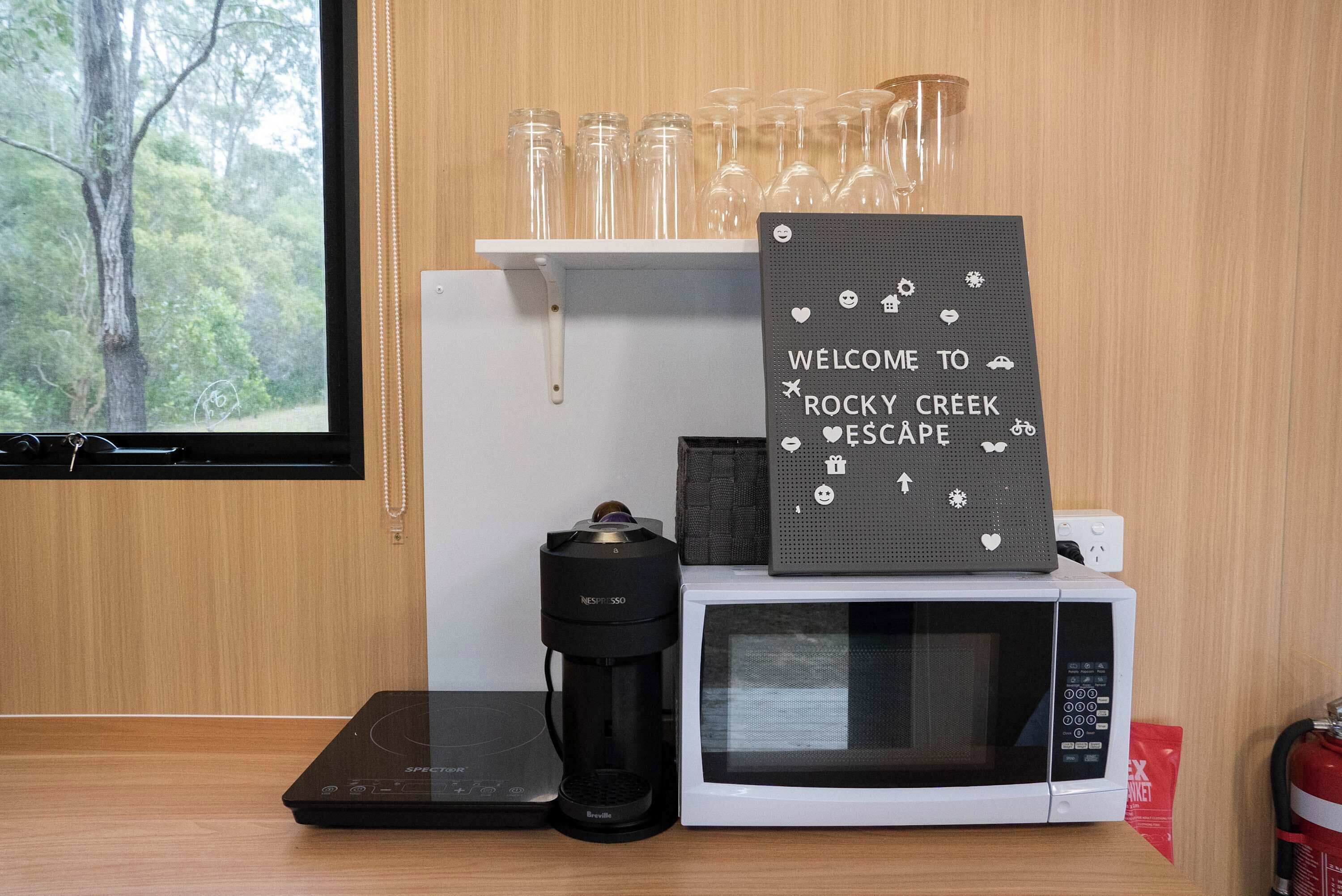 Un área de cocina con cafetera, microondas y un letrero que dice "WELCOME TO ROCKY CREEK ESCAPE".