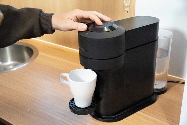 A person operating a black coffee machine with a white mug on a coaster.