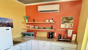 A compact kitchen with white cabinets, a microwave, a coffee maker, and a teal table. - Fossil Knob Ridge -Sierra Vista: Ultra Modern (Terlingua)